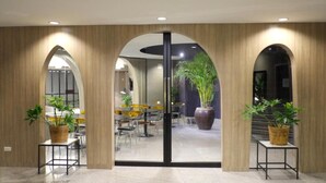 Un intérieur moderne avec des murs lambrés en bois, une porte d’entrée en verre et des plantes en pot de chaque côté.