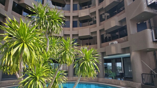 Un bâtiment moderne doté d’une piscine centrale, entourée de palmiers.