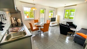 A modern kitchen with a dining area, a TV, and a sofa. - 05 Ferienwohnung Greta mit Balkon - Appartementhaus Greta im Ostseebad (Sellin)