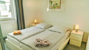 A double bed with patterned bedding, two bedside tables with lamps, a window with curtains, and a framed picture on the wall. - 05 Ferienwohnung Greta mit Balkon - Appartementhaus Greta im Ostseebad (Sellin)