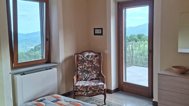 Une chambre à coucher avec un grand lit, une chaise, une commode, un lustre et une vue par les fenêtres.