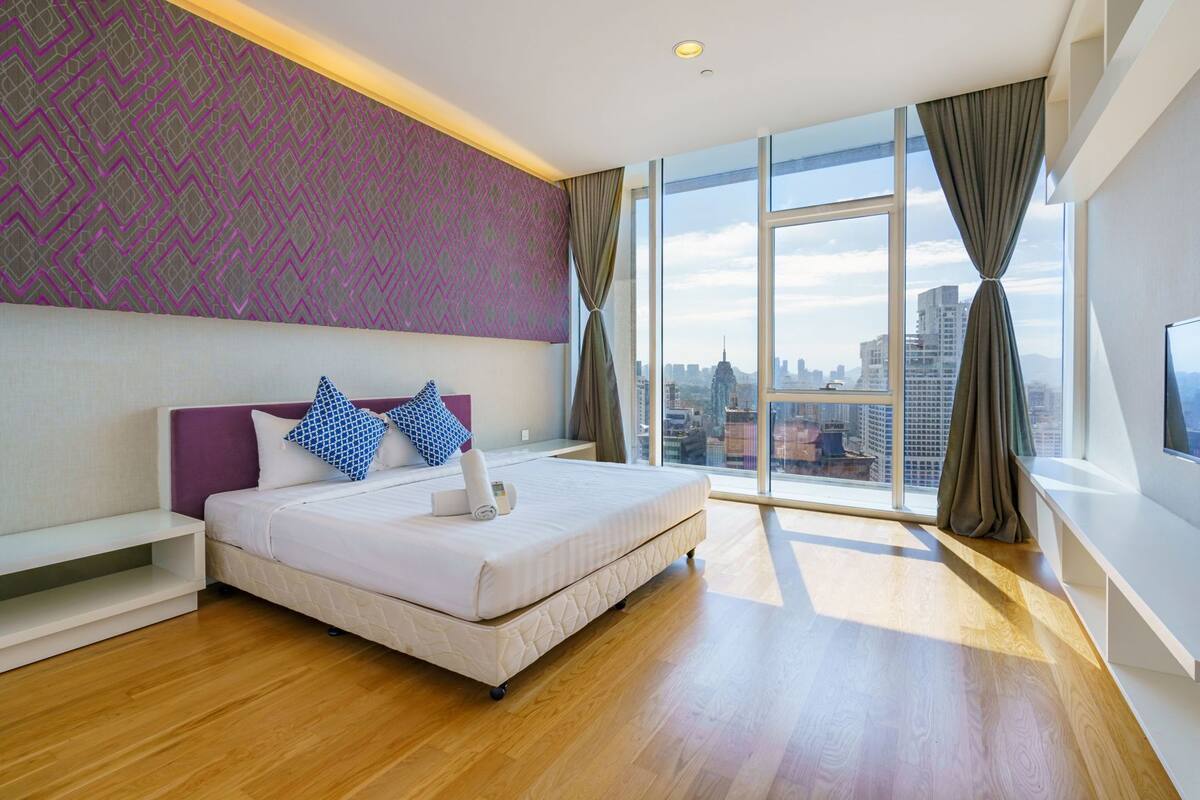 A modern hotel room with a large bed, a city view, and a patterned wall.