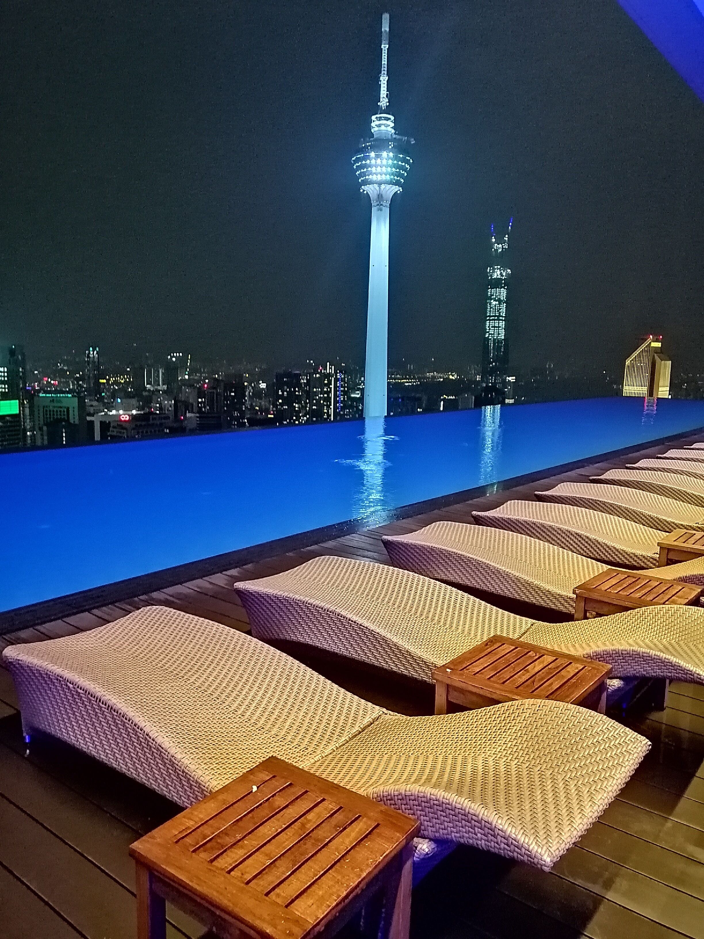 A rooftop pool area with lounge chairs and a city skyline view at night.