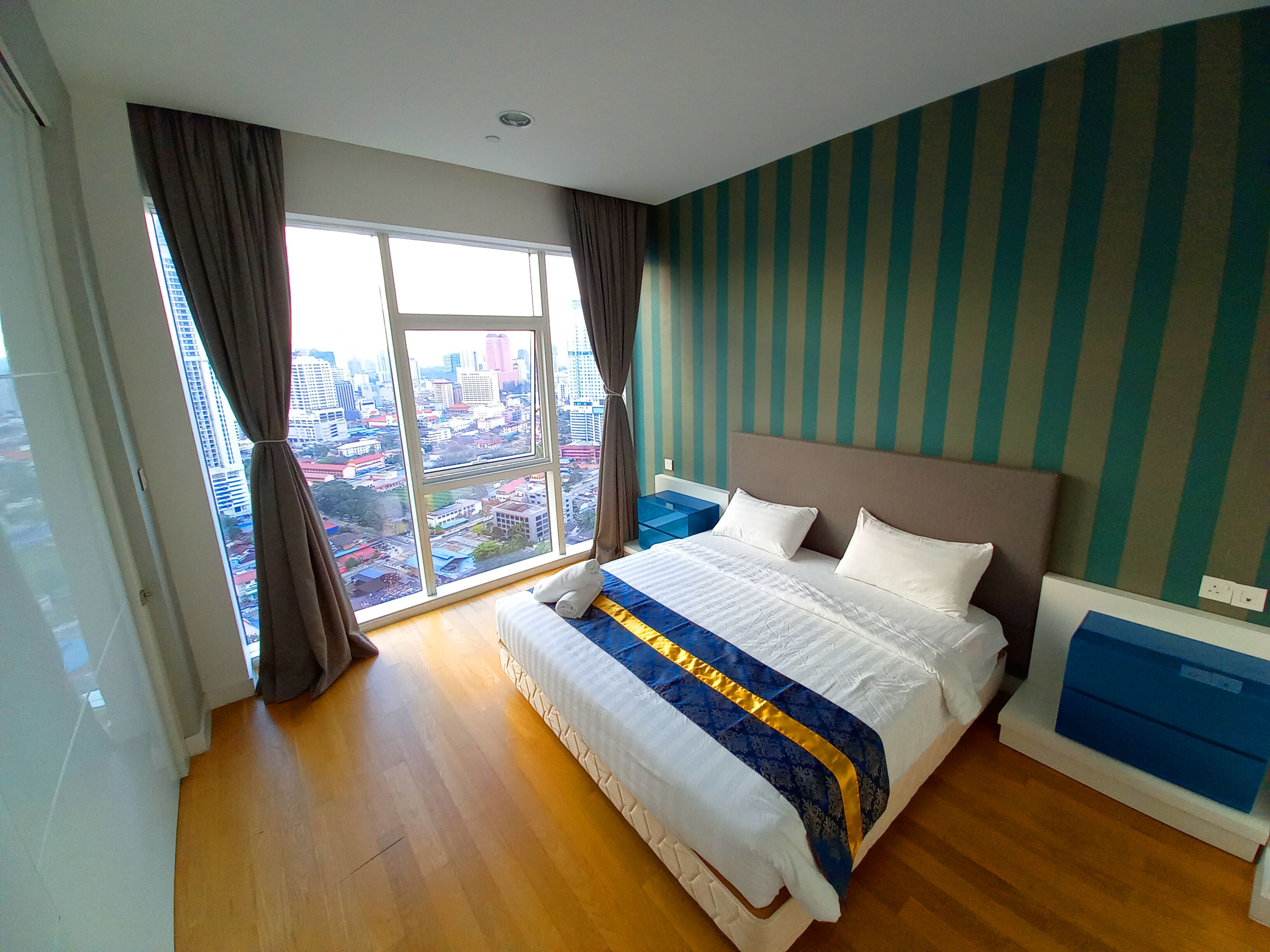 A bedroom with a large bed, a view of the city through a window, and a striped wall.