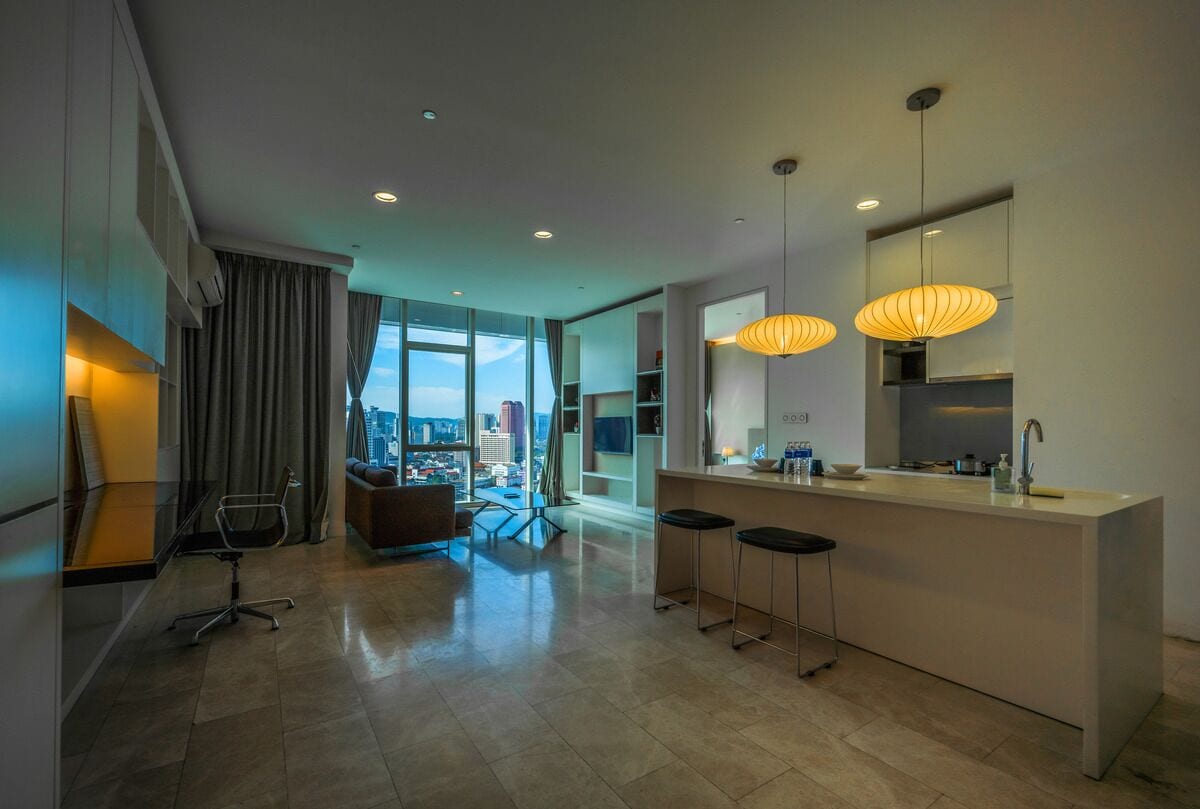 A modern kitchen with a large island, bar stools, pendant lights, and a view of the city.