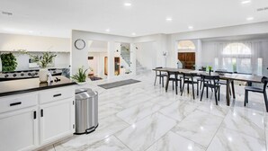 Een moderne keuken met witte kasten, een marmeren aanrechtblad en een eethoek met een grote tafel en stoelen.