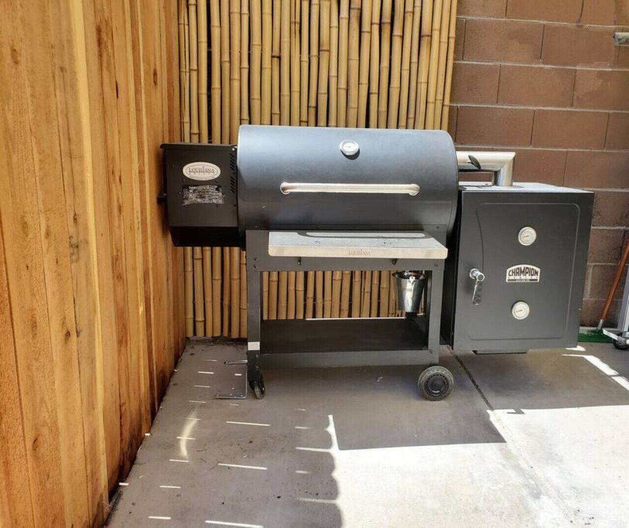 A charcoal grill with a side cabinet, positioned against a bamboo wall and brick wall.