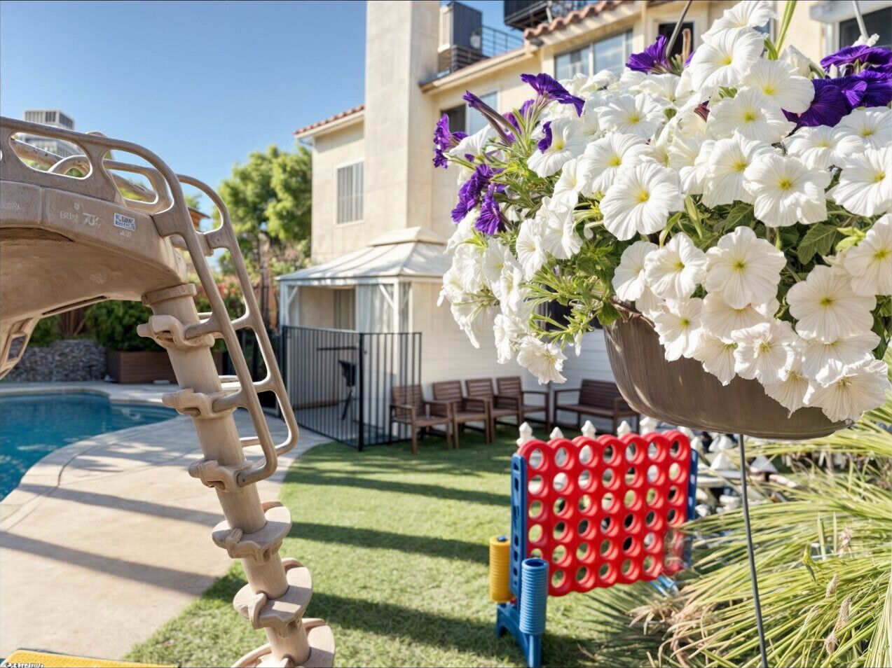 A poolside area with a metal ladder, a hanging flower arrangement, and outdoor furniture.