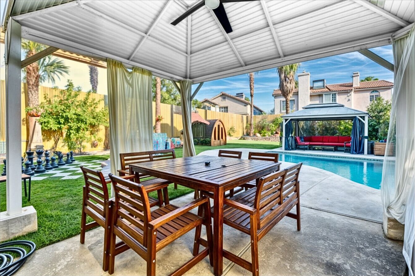 A covered patio with a pool, wooden furniture, and a chessboard.