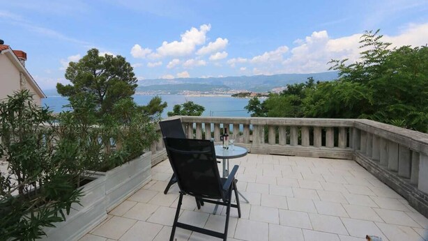 A patio with a table and chair, overlooking a scenic view of a body of water and distant land. - Apartment Dunato Nedeljko B2 (Silo - island Krk)