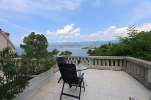 A patio with a table and chair, overlooking a scenic view of a body of water and distant land. - Apartment Dunato Nedeljko B2 (Silo - island Krk)