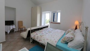 A bedroom with a bed, a chair, a table, a TV, and a window. - Apartment Dunato Nedeljko B2 (Silo - island Krk)