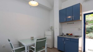 A compact kitchen with a table and chairs, a refrigerator, and blue cabinets. - Apartment Dunato Nedeljko B2 (Silo - island Krk)