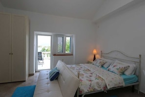 A bedroom with a bed, a sofa, a lamp, a window, and a door.