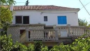 A two-story building with a tiled roof, a blue door, and a stone facade. - Apartment Dunato Nedeljko B2 (Silo - island Krk)