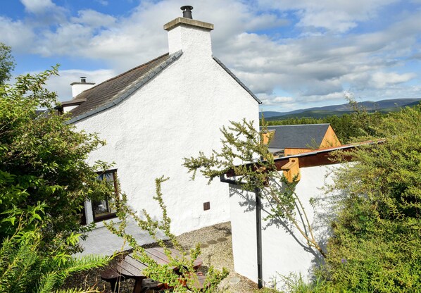A white building with a sloped roof, a chimney, and a window. - A home in the Scottish Highlands. (Dulnain Bridge)
