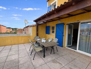 Een terras met een tafel gedekt voor vier personen, een blauwe deur en een schotelantenne.