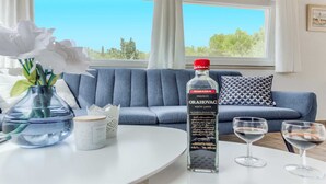 Una sala de estar moderna con un sofá azul, una mesa de vidrio con un jarrón de flores, una botella de licor y dos copas de vino.