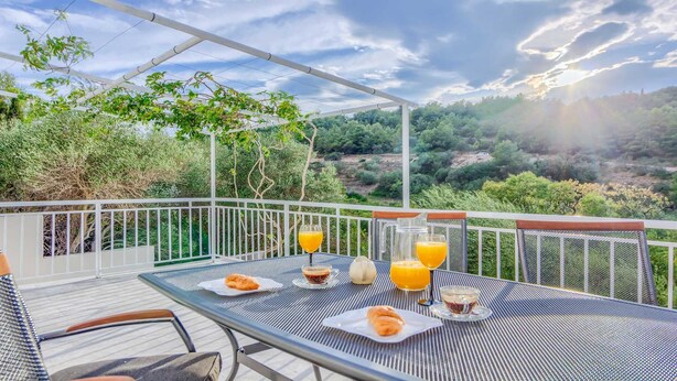 Una terraza con una mesa dispuesta para el desayuno, que incluye cruasanes y jugo de naranja, con vistas a un paisaje pintoresco.
