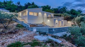 Una casa moderna de dos pisos con un balcón, una escalera que lleva a la entrada y un exterior bien iluminado.