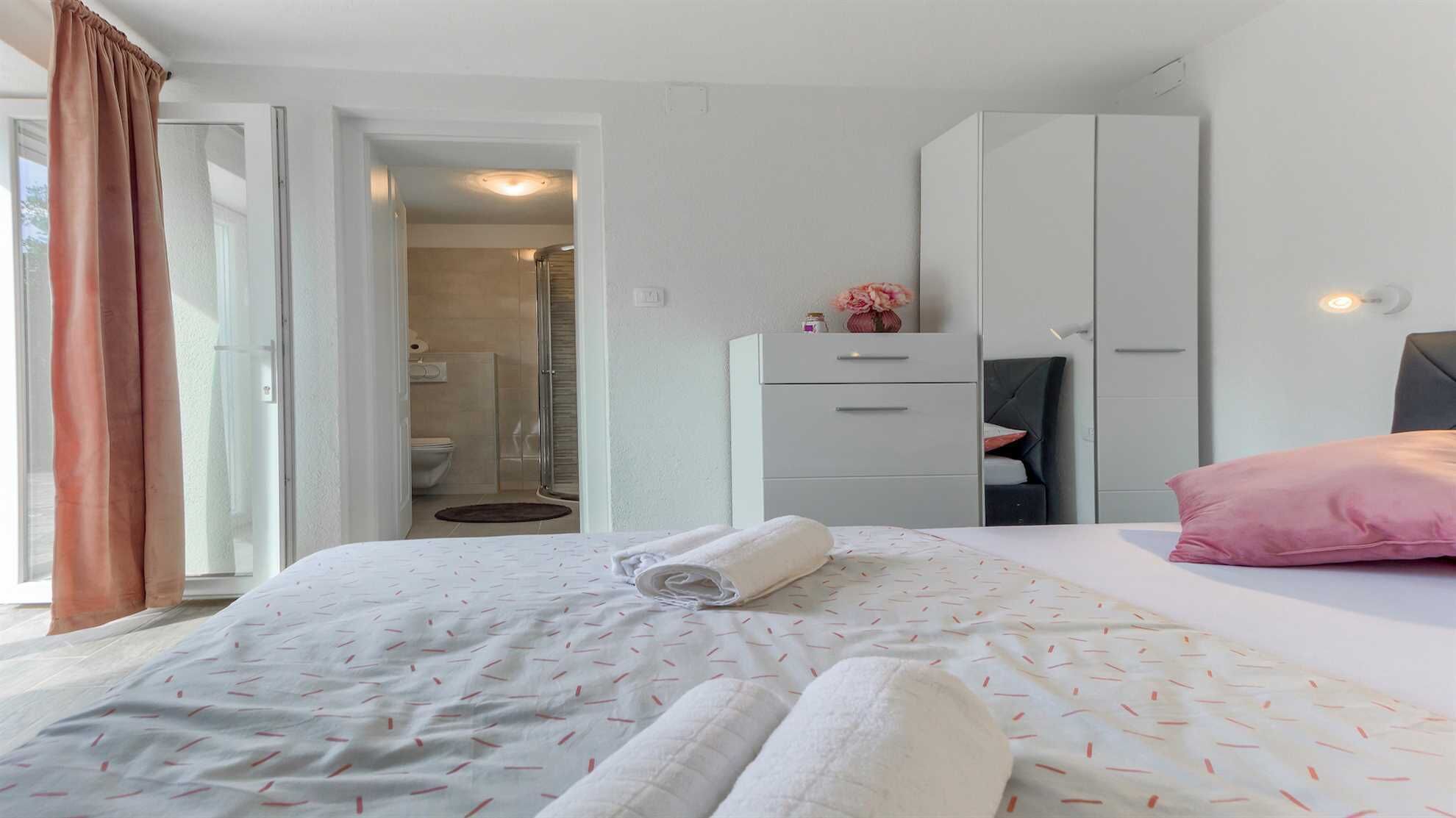A hotel room with a bed, a wardrobe, a desk, and a bathroom visible through an open door.