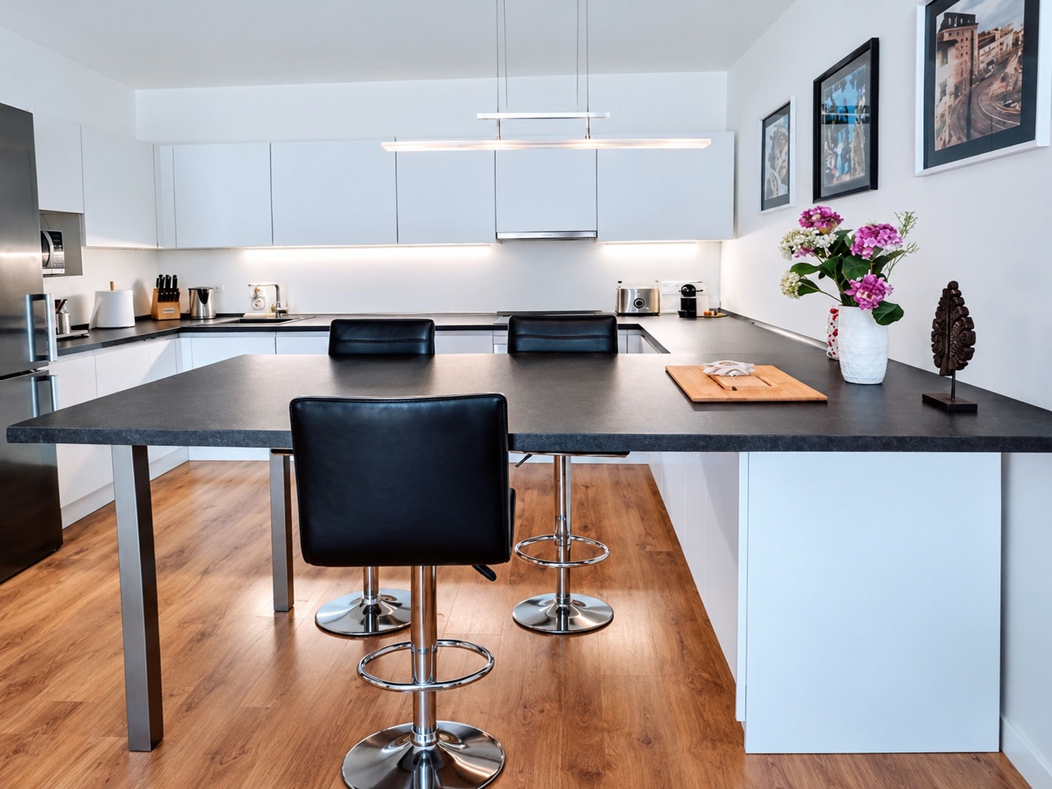 A modern kitchen with a central island, bar stools, and a vase with flowers.
