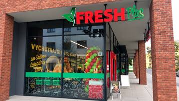 En butik med en stor glasfasad, en skylt med texten ”FRESH Plus” och en uppsättning färgglada ballonger som dekor.
