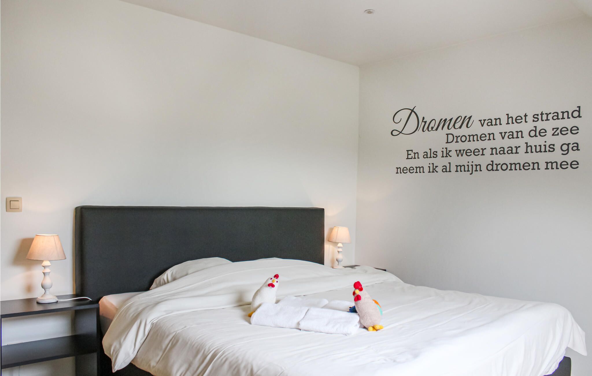 Una camera d'albergo con un letto grande, due abat-jour e una parete con un testo in olandese.