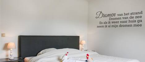 A hotel room with a large bed, two bedside lamps, and a wall with a Dutch text.