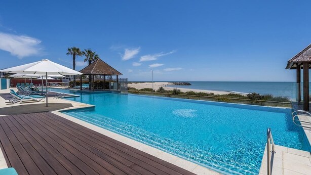 A clear blue pool with a wooden deck, lounge chairs, and a beach view. - Stunning 270 degrees view of the Ocean, Beach & Marina Views (mandurah)