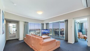 A modern living room with a large sofa, a flat-screen TV, and a balcony with a view. - Stunning 270 degrees view of the Ocean, Beach & Marina Views (mandurah)