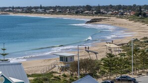 A beach with a lifeguard tower, a sandy shore, and a residential area in the background. - Stunning 270 degrees view of the Ocean, Beach & Marina Views (mandurah)