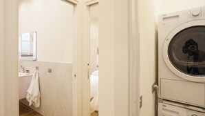 Un área de lavandería con lavadora y secadora, un baño con espejo y lavamanos, y piso de madera.