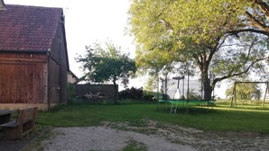 Un patio trasero con un trampolín, un banco de madera y un árbol.