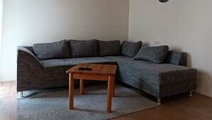 Una sala de estar moderna con techo de madera, un sofá seccional gris y una pequeña mesa de madera.