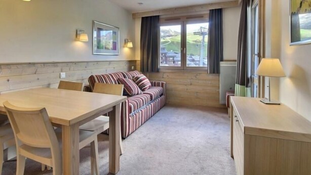 Een gezellige kamer met een houten eettafel, een gestreepte bank en een raam met uitzicht op de omgeving.