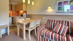 Een ruimtelijk ingerichte leefruimte met een eethoek, kitchenette en een bank met gestreepte kussens.