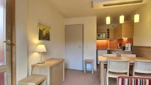 Een compacte hotelkamer met een kitchenette, een eethoek met tafel en stoelen, en een klein zithoekje met een gestreept sofa.