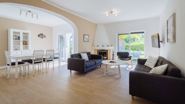 A spacious living area with a dark sofa, white dining table, and chairs. There is a fireplace and a large window providing natural light. - Top renovated townhouse with pool and sea access (Porches)