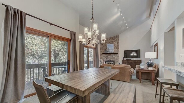 Amplia sala de estar con mesa de comedor de madera, asientos cómodos, chimenea de piedra y un ventanal con vista a árboles.