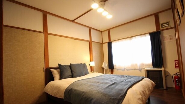 A hotel room with a bed, a window with curtains, a ceiling fan, and a wall-mounted air conditioning unit.