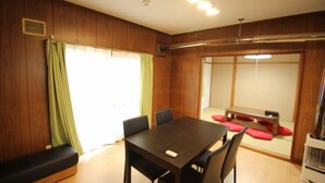 A room with a wooden paneled wall, a dining table with chairs, a bench, and a sliding door leading to another room.