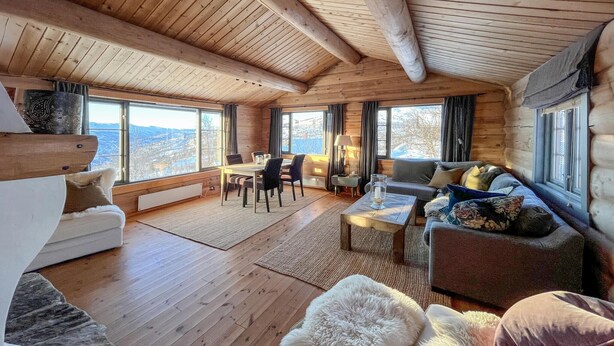 A log cabin interior with a dining area, sofa, and large windows offering a view. - 3 bedroom amazing home in Uvdal (Uvdal)