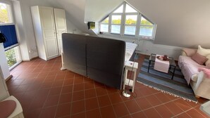 Ein kompakter Wohnraum mit Küchenzeile, einer Couch, einem Esstisch und Seeblick durch große Fenster.