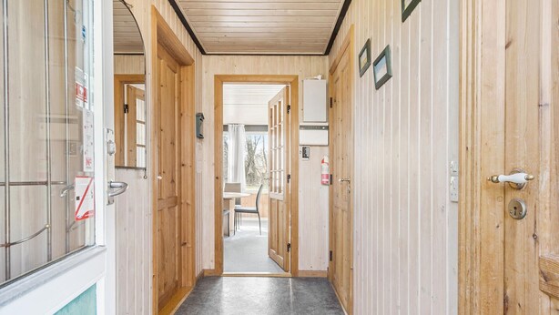 En korridor med trædøre, en grå gulv og udsigt til et udendørs område med et bord og stole.
