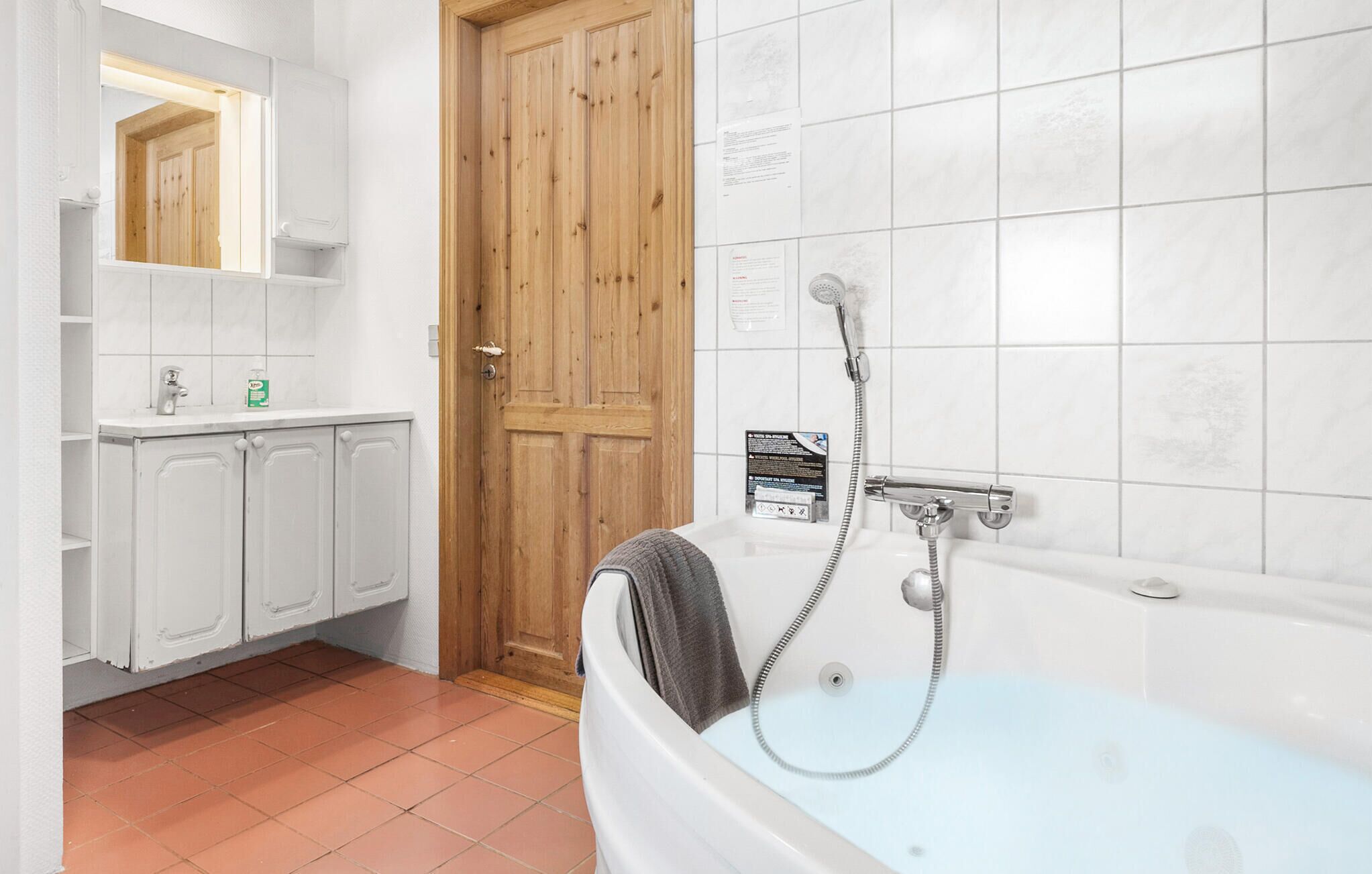 A bathroom with a bathtub, a wooden door, a mirror, and a white sink with a soap dispenser.