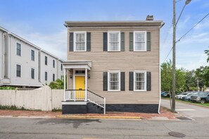 A two-story house with a front porch, a yellow door, and a black front step.