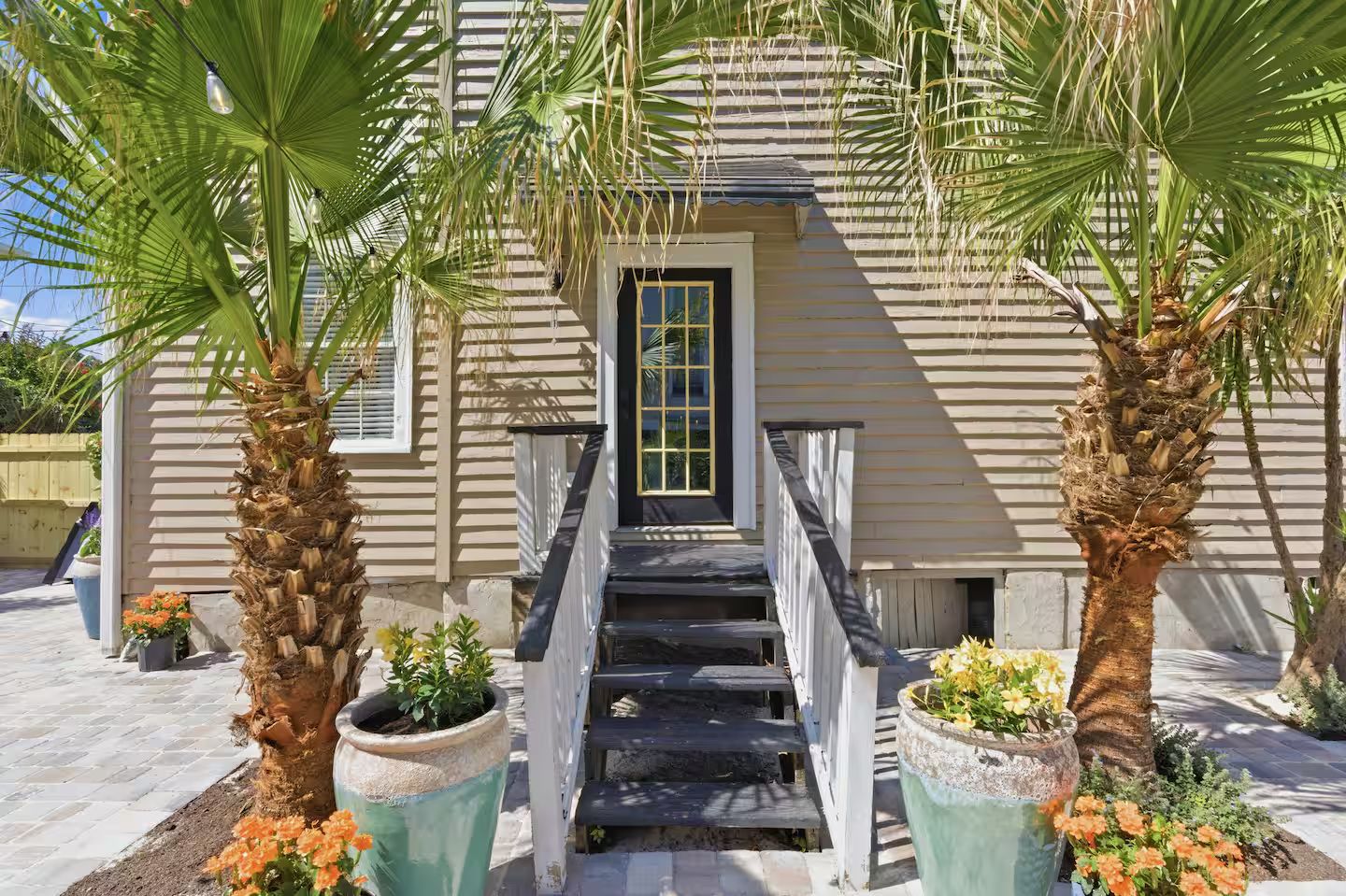 Une maison avec un porche à l’avant, un escalier et des plantes en pot.