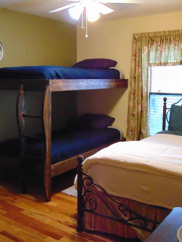 A room with bunk beds, a single bed, a wooden floor, a ceiling fan, and a window with floral curtains. - Luxury Home on The Weeki Wachee River! (Spring Hill)