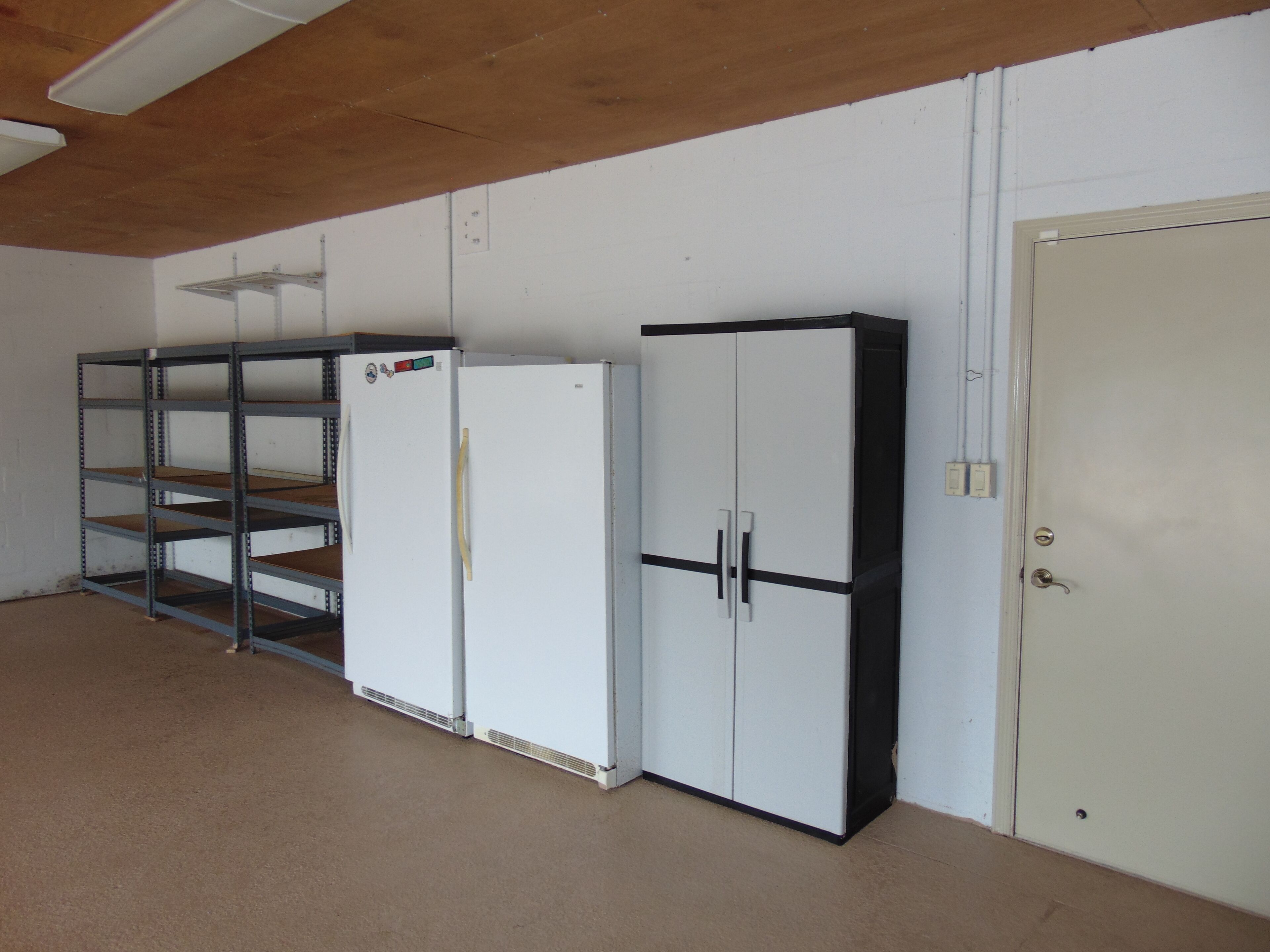 Una habitación con una puerta blanca, un refrigerador blanco y una estantería metálica.